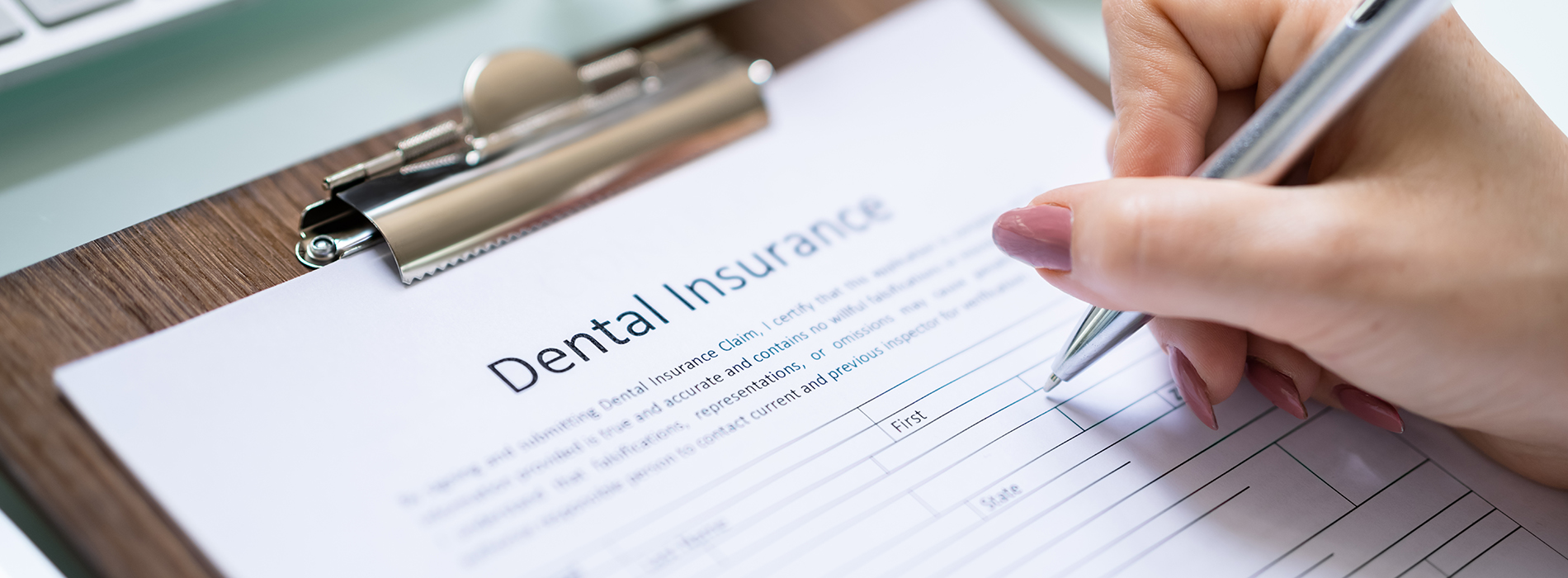 A person s hand holding a pen above a clipboard with a form titled Dental Insurance , displaying the words Insurance Information and Dentist .